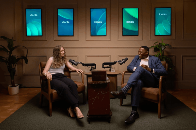 John and Charlotte sitting in a podcast recording room. The image with a play button on it to launch a video
