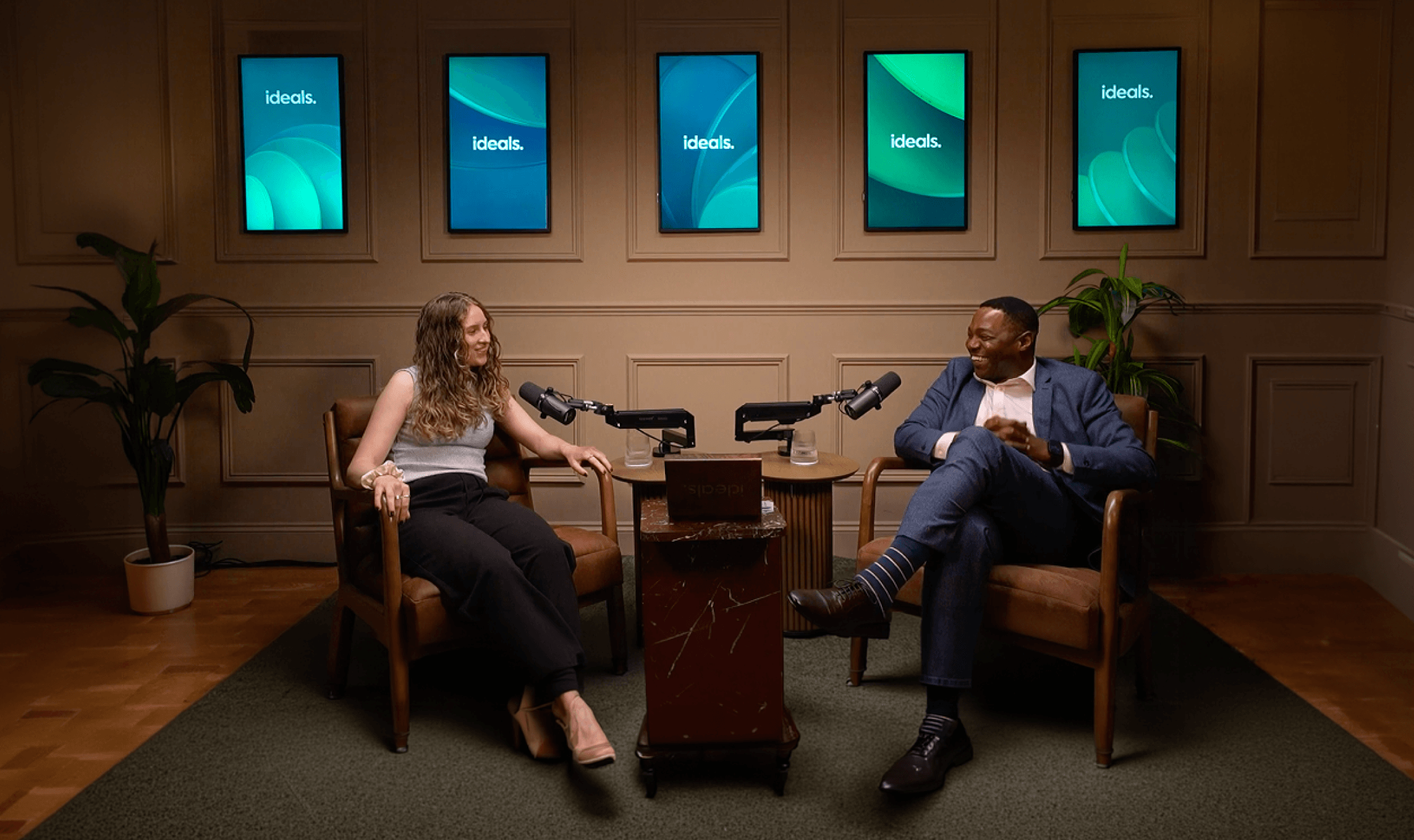 John and Charlotte sitting in a podcast recording room. The image with a play button on it to launch a video